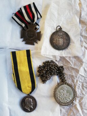 Zwei Orden und zwei Medaillen. Eine Medaille hängt an einer Kette, an den beiden Orden sind Ordensbänder befestigt.