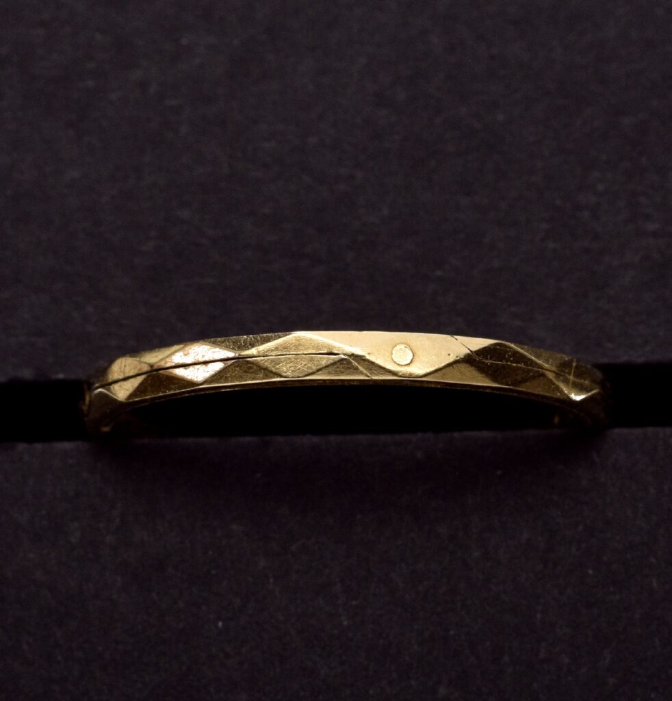 Ein schmaler goldfarbener Ring, der von einer feinen Längslinie durchtrennt wird.