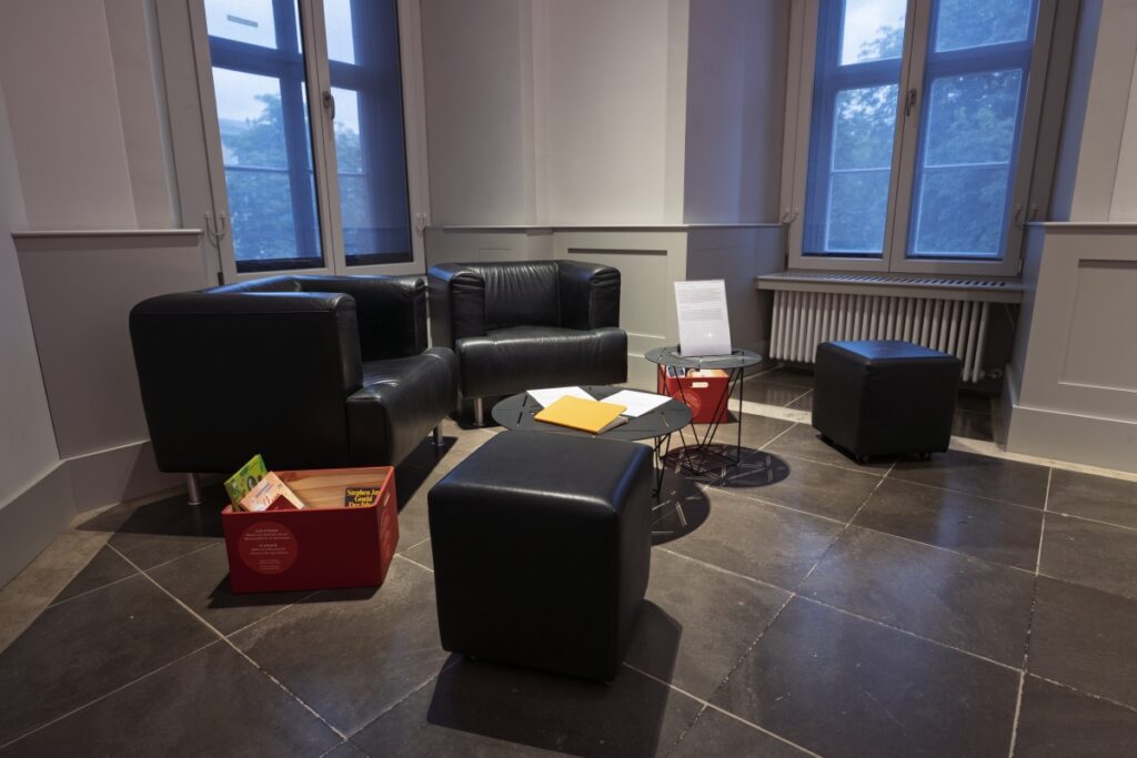 Schwere, schwarze Polstermöbel um eine Tischgruppe und Kisten gefüllt mit Büchern.