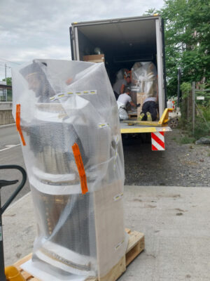 Große, in Luftpolsterfolie eingepackte Skulptur steht auf einer Palette vor einem LKW.
