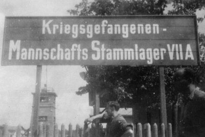 Schwarz-weiß-Fotografie eines Schildes mit der Aufschrift „Kriegsgefangenen - Mannschafts Stammlager VII A“.