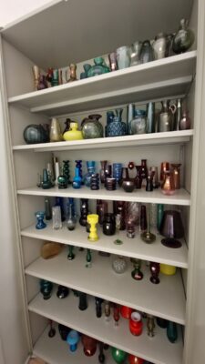 Verschiedenfarbige Glasobjekte in einem Schrank in Regalfächern.