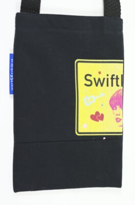 Kleine, schwarze Tasche mit einem gelben Aufdruck, der ein zur Hälfte angeschnittenes Ortsschild, dekorative Elemente und ein Gesicht darstellt.