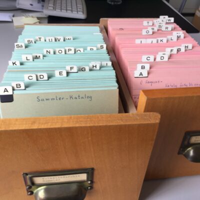 Blick in zwei Zettelkästen, einer enthält blaue, der andere rosa Karten. Man kann das Register sehen.