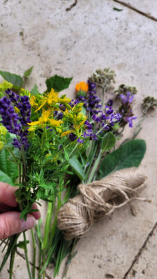 Eine Hand hält eine Blume, im Hintergrund ist ein Blumenstrauß zu sehen.