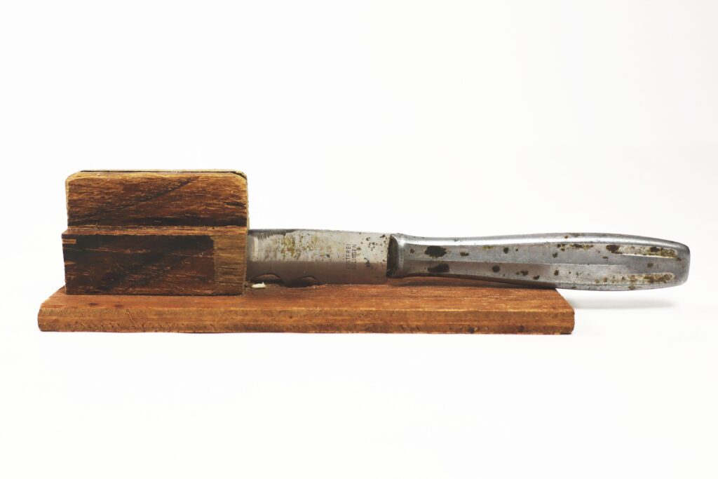 Ein Buttermesser aus Metall. Die Klinge wurde zwischen Holzklötzchen befestigt, man kann damit Nüsse öffnen.