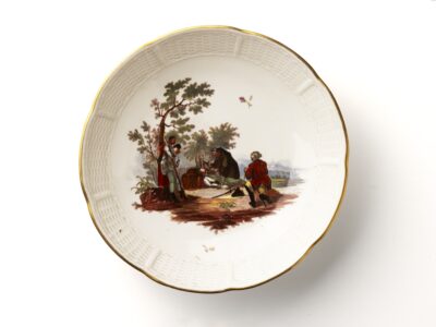 Blick auf eine helle Untertasse mit regelmäßigem leicht verbogenem Rand und Malerei in der Mitte.