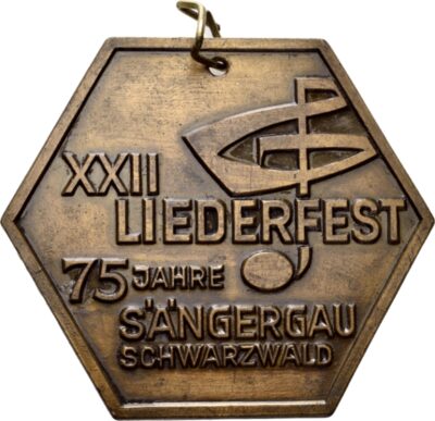 Eine sechseckige Medaille mit einem Notenschlüssel und der Inschrift: "XXII LIEDERFEST 75 JAHRE SÄNGERGAU SCHWARZWALD".