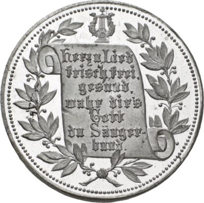 Eine Münze mit einem gerollten Schriftband, das von Zweigen ein gerahmt wird. Auf dem Schriftband steht die Inschrift: "Herz u. Lied / frisch, frei, / gesund, / wahr dirs / Gott / du Sänger- / bund."