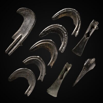 Neun Objekte aus Bronze vor einem schwarzen Hintergrund. Dazu gehören ein Sichelmesser, fünf Sicheln und drei Beile.